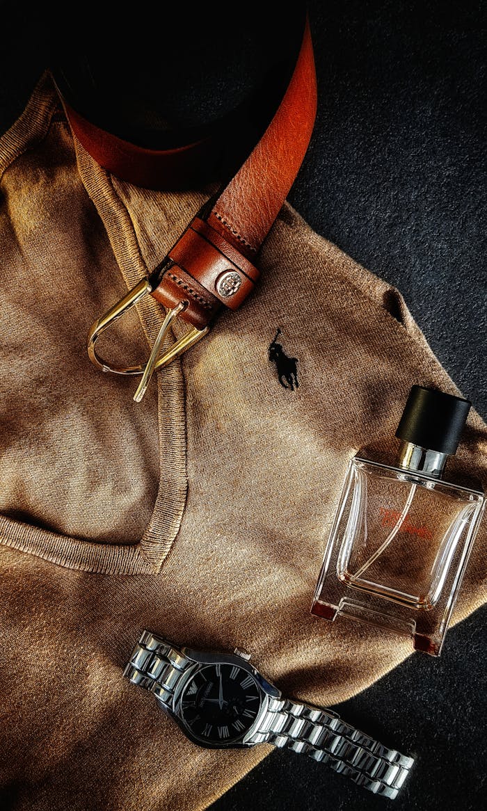 Stylish flat lay featuring a brown sweater, leather belt, wristwatch, and fragrance bottle.